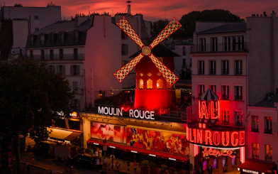 Moulin Rouge illuminated at sunset in Paris, featuring iconic red windmill.