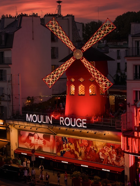 Moulin Rouge illuminated at sunset in Paris, featuring iconic red windmill.