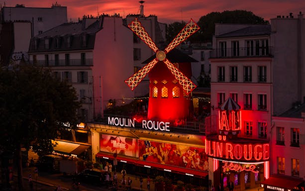 Moulin Rouge illuminated at sunset in Paris, featuring iconic red windmill.