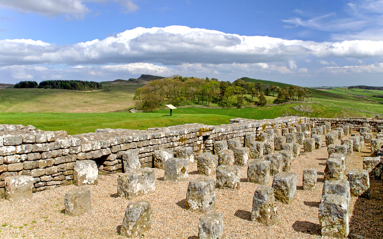 Housesteads Roman Fort ruins with stone walls and green landscape in Northumberland, England.