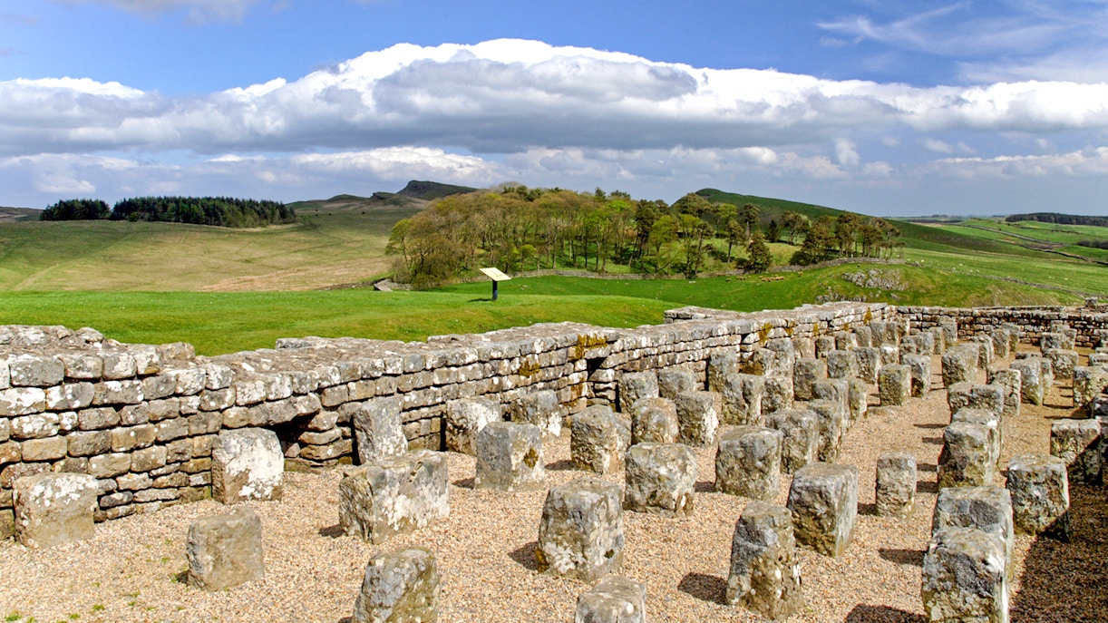 Housesteads Roman Fort ruins with stone walls and green landscape in Northumberland, England.