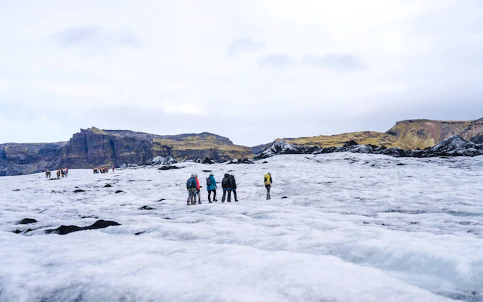 Guests hiking on Sólheimajökull Glacier in Iceland with distant mountains.