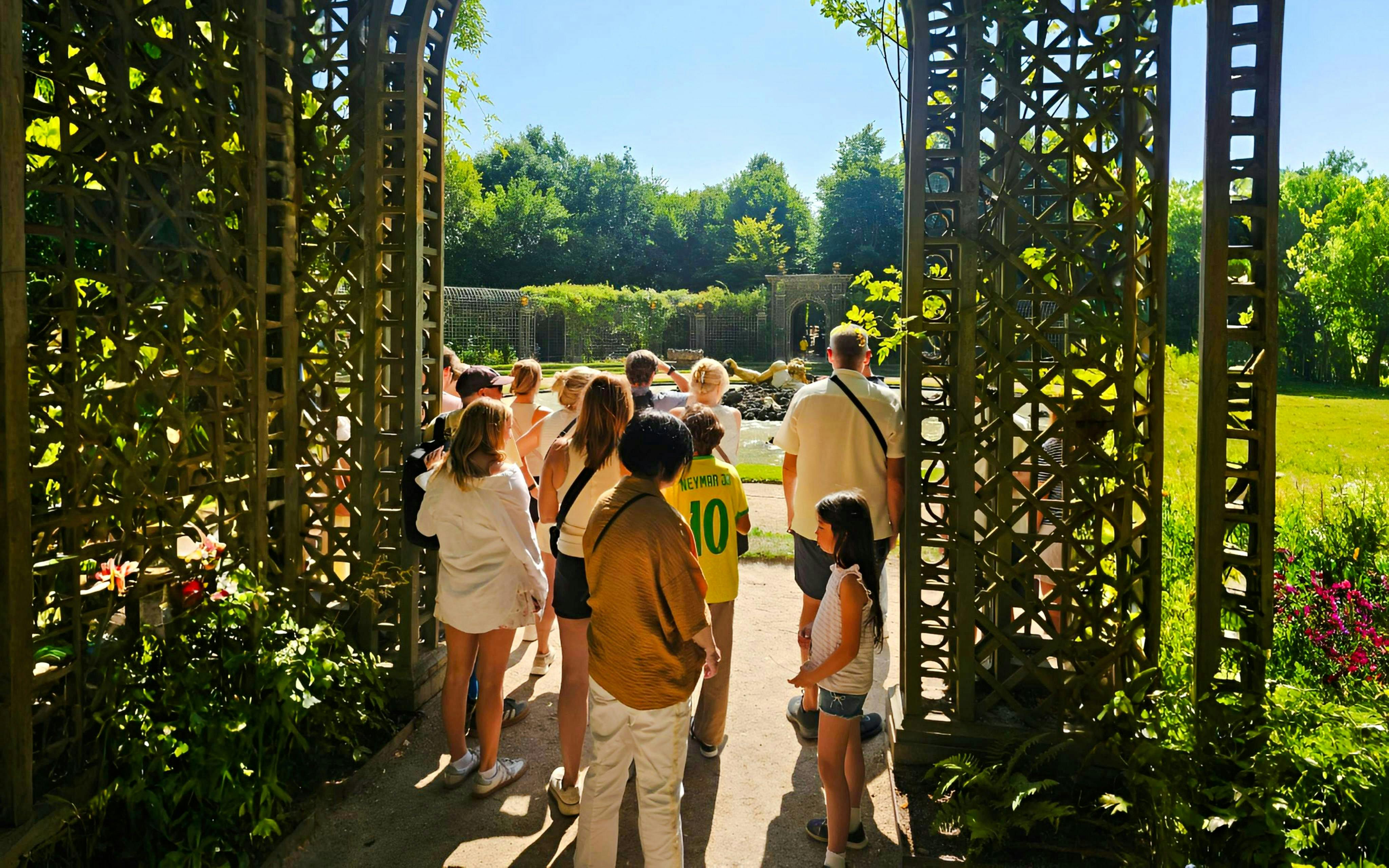 Group touring Versailles gardens through ornate gate.