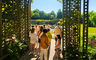 Group touring Versailles gardens through ornate gate.