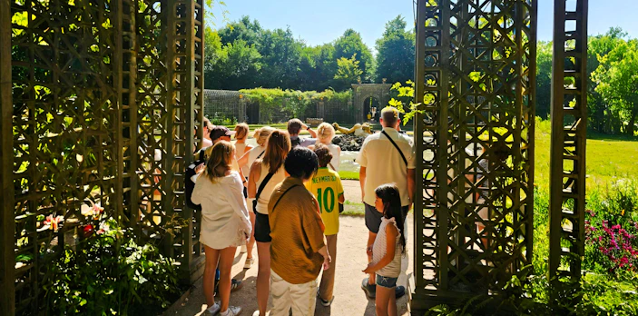 Group touring Versailles gardens through ornate gate.