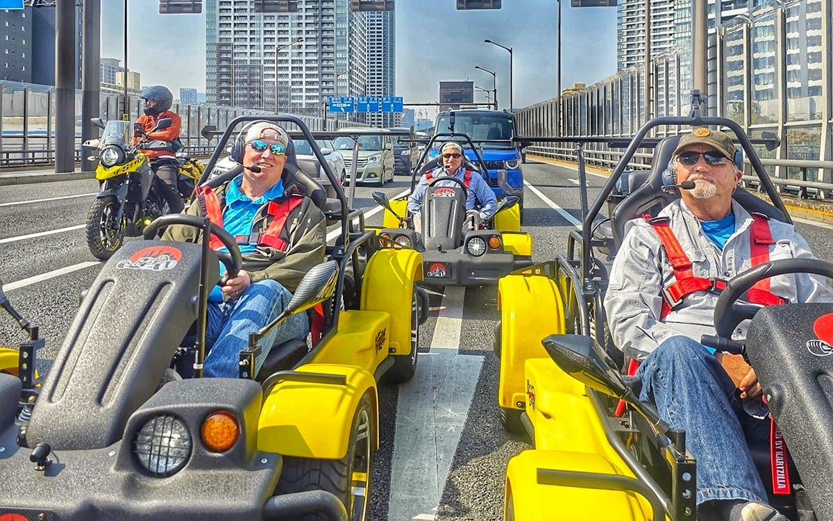 Go-kart riders on Tokyo street tour with city skyline in background.