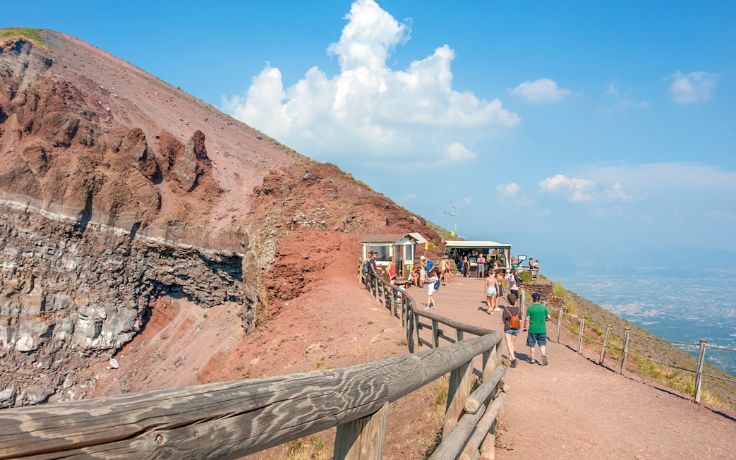 Visitors walking along the Mount Vesuvius crater path with a view of Naples.