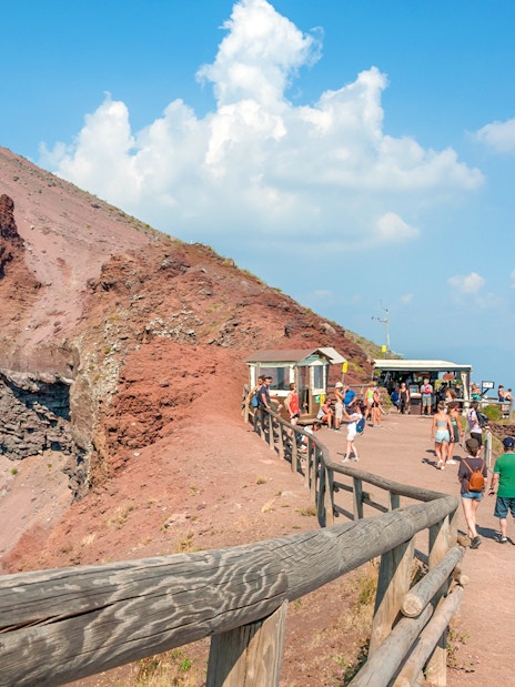 Visitors walking along the Mount Vesuvius crater path with a view of Naples.