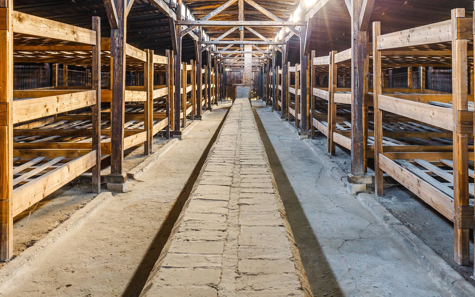 Interior of Auschwitz Birkenau barracks with wooden bunks and central walkway.