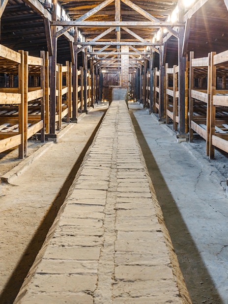 Interior of Auschwitz Birkenau barracks with wooden bunks and central walkway.