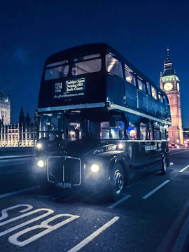 Vintage double-decker bus on London ghost tour near Big Ben at night.