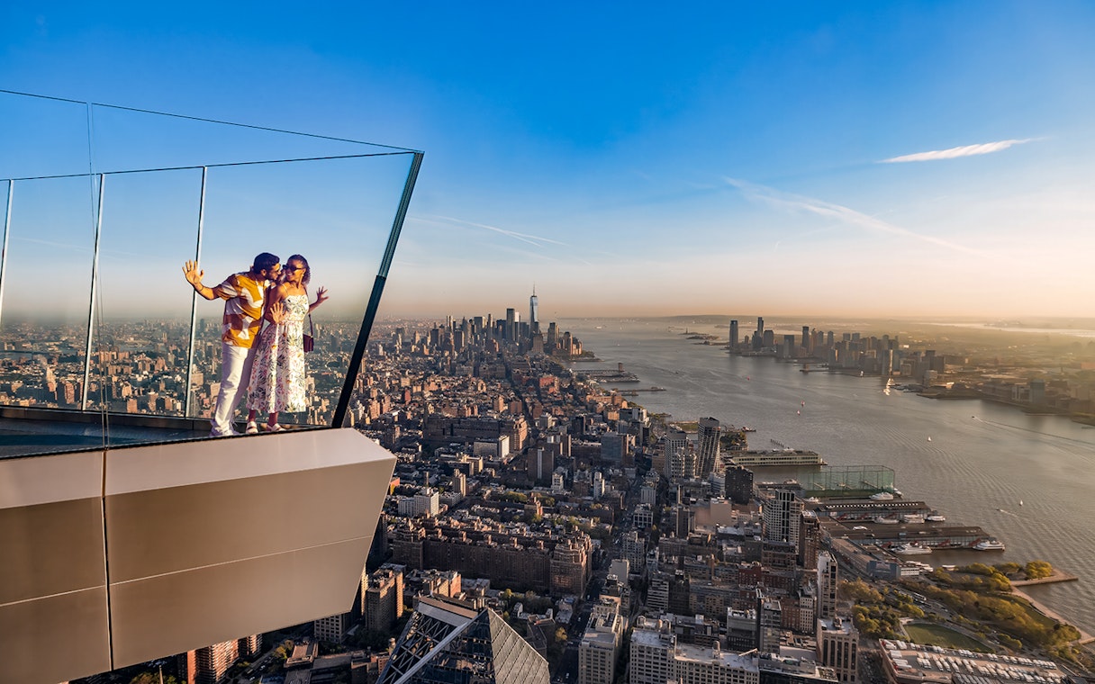 Couple enjoying view from the western overhang of the Edge Observation Deck, New York City skyline in background.