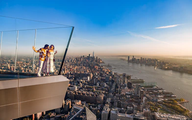 Couple enjoying view from the western overhang of the Edge Observation Deck, New York City skyline in background.