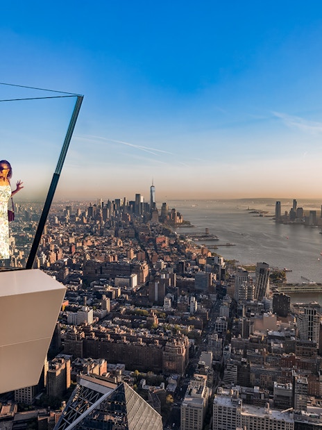 Couple enjoying view from the western overhang of the Edge Observation Deck, New York City skyline in background.
