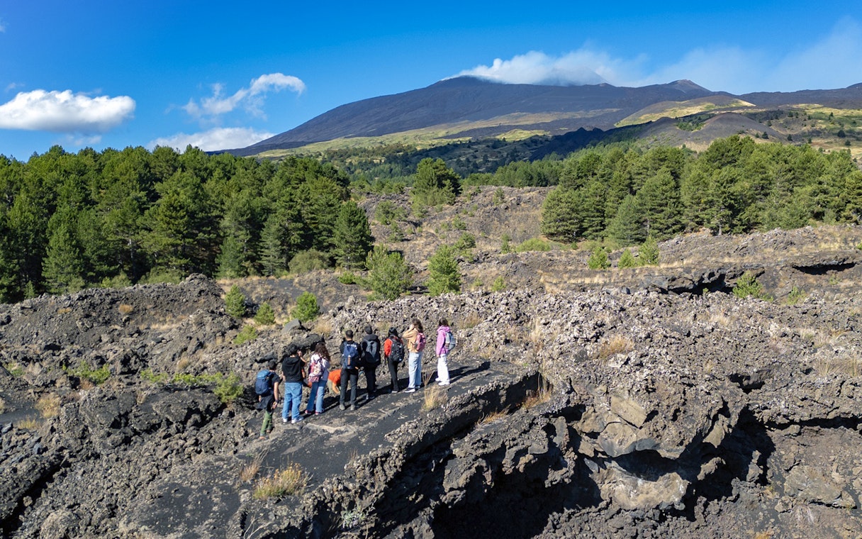 Tourists exploring lava caves near Mount Etna with forested landscape.