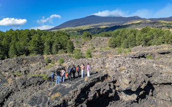 Tourists exploring lava caves near Mount Etna with forested landscape.