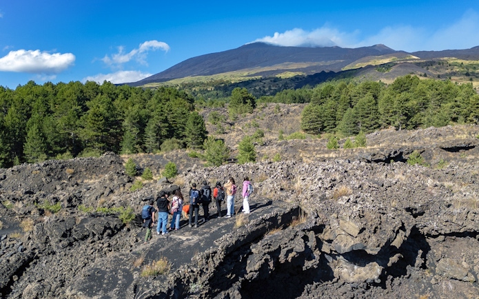 Tourists exploring lava caves near Mount Etna with forested landscape.
