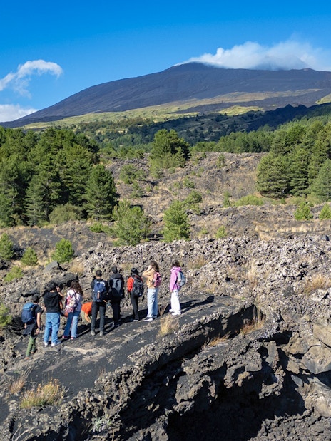 Tourists exploring lava caves near Mount Etna with forested landscape.