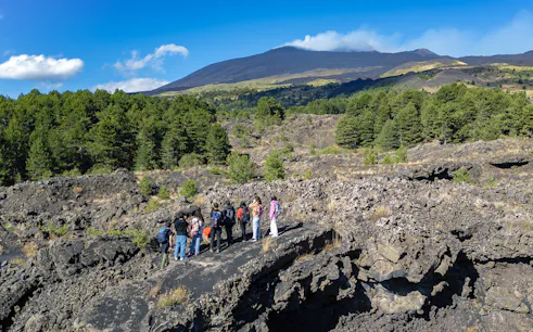 Tourists exploring lava caves near Mount Etna with forested landscape.