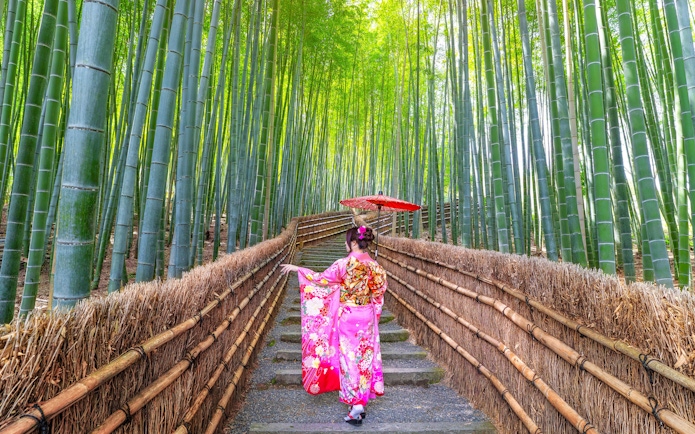 Person in traditional kimono walking through Arashiyama Bamboo Grove, Kyoto, Japan.