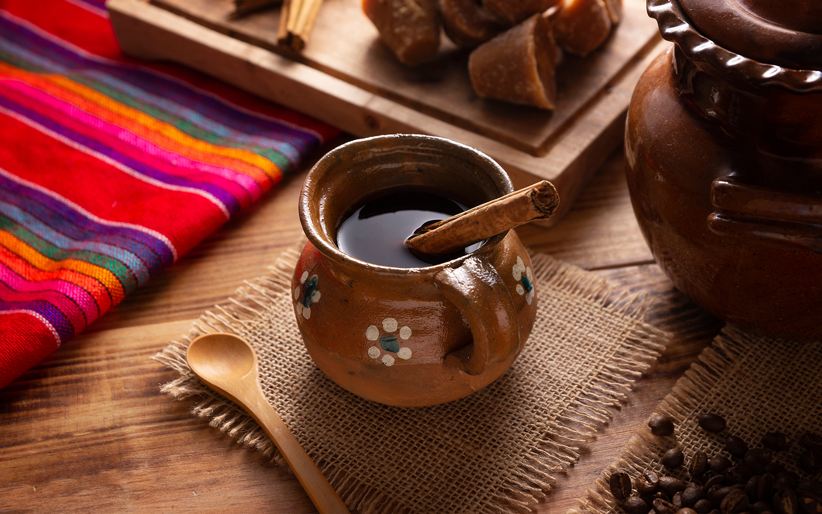 Cafe de Olla in a clay jarrito with cinnamon and piloncillo on a rustic wooden table.