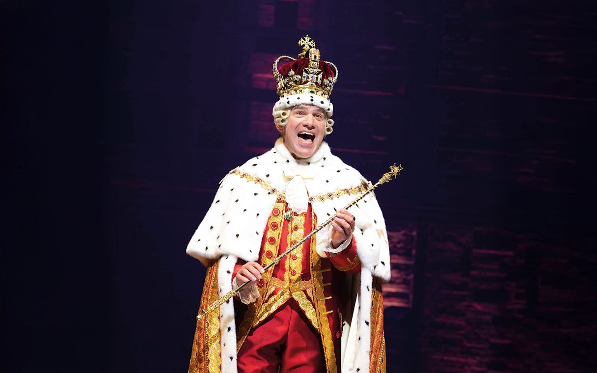 Performer in royal costume during Hamilton musical scene.