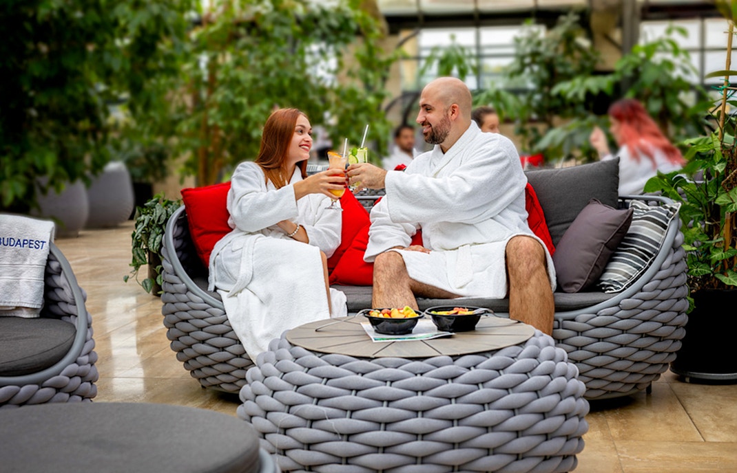 Guests enjoying drinks inside Szechenyi Bath Palm House, Budapest, surrounded by lush greenery.
