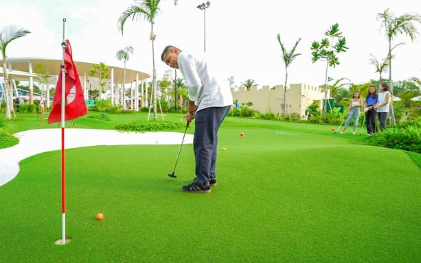Man playing mini-golf on green course with friends watching, part of Combo: HyperDrive and UltraGolf experience.