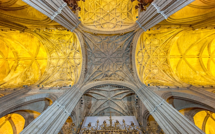 Seville Cathedral's ornate ceiling and arches, showcasing intricate Gothic architecture.