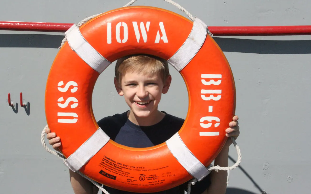 Boy smiling through USS Iowa BB-61 lifebuoy on self-guided tour.