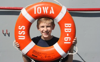 Boy smiling through USS Iowa BB-61 lifebuoy on self-guided tour.