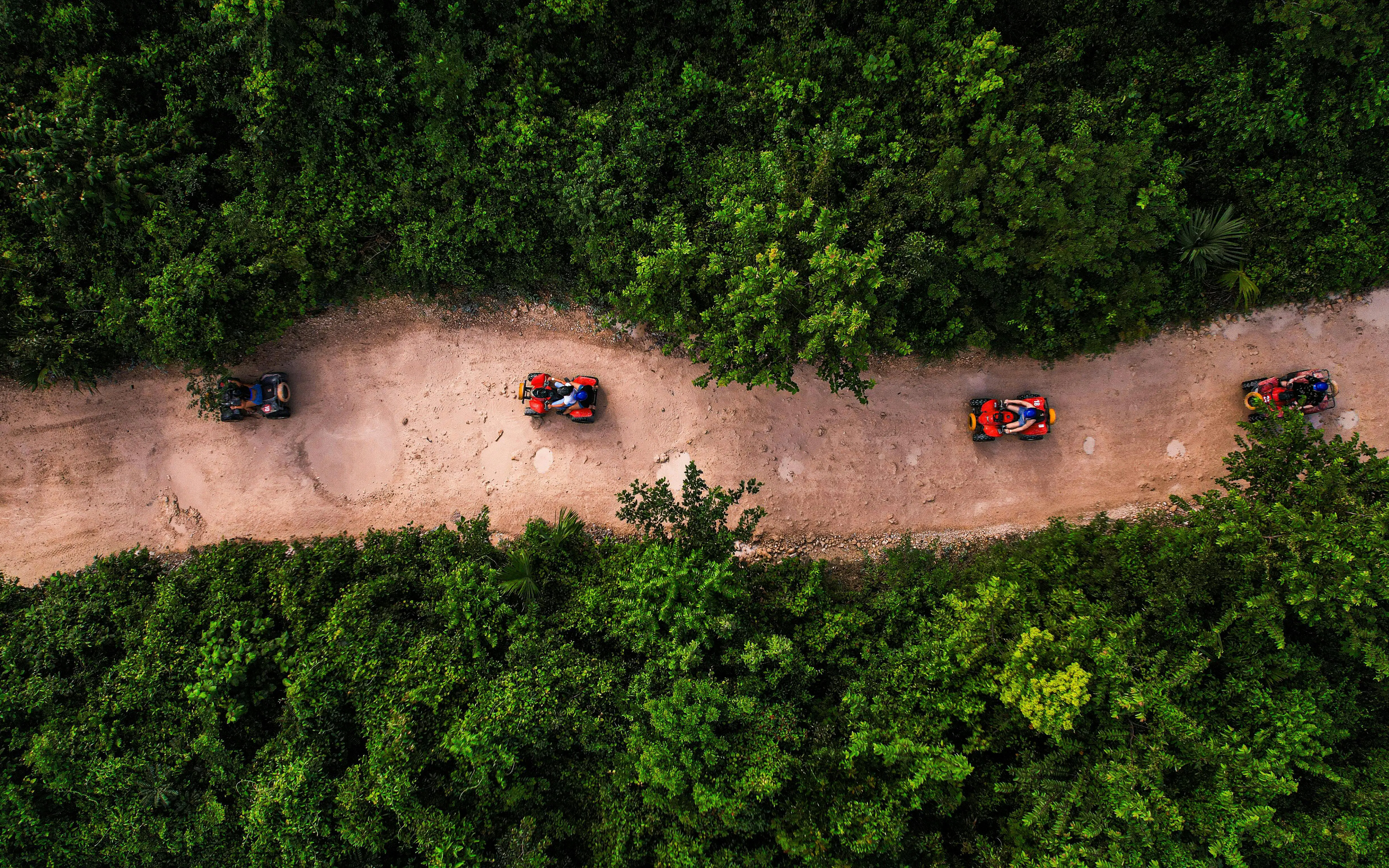 ATVs on a dirt path through lush greenery at Cancun Extreme Adventuring Park.