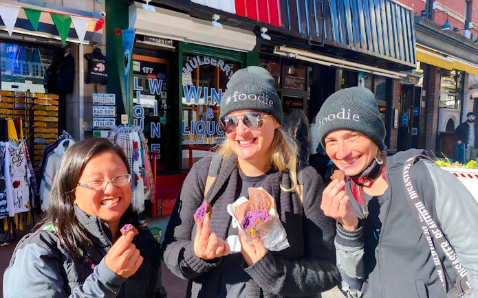 Tourists savoring crepes at Ahoy New York Food Tours in front of a local shop.