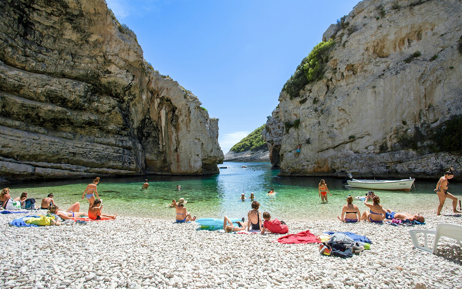 Visitors relaxing on the pebble beach at Stiniva Cove, Vis Island, Croatia.