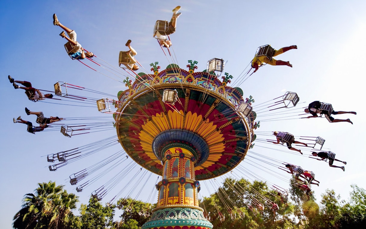 Colorful swing ride at Isla Mágica theme park, Seville, with people enjoying the attraction.
