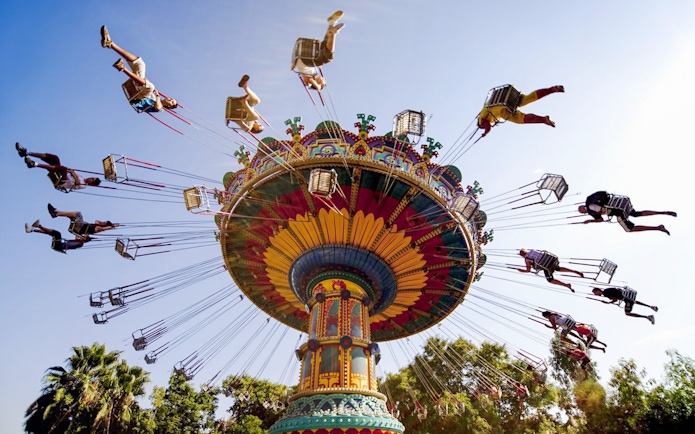 Colorful swing ride at Isla Mágica theme park, Seville, with people enjoying the attraction.