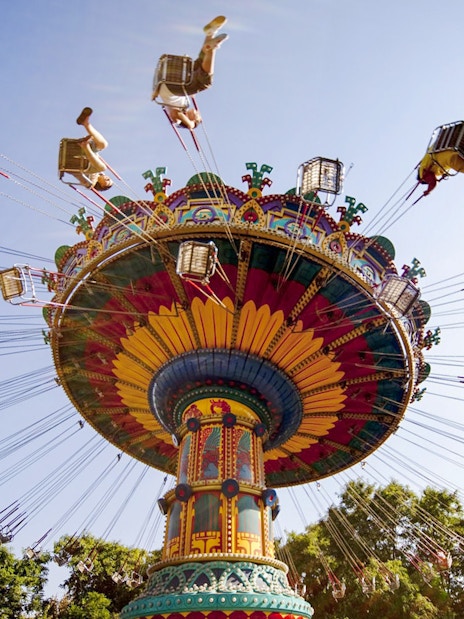 Colorful swing ride at Isla Mágica theme park, Seville, with people enjoying the attraction.