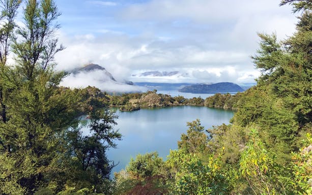 Mou Waho Island lake view with surrounding greenery and distant mountains.