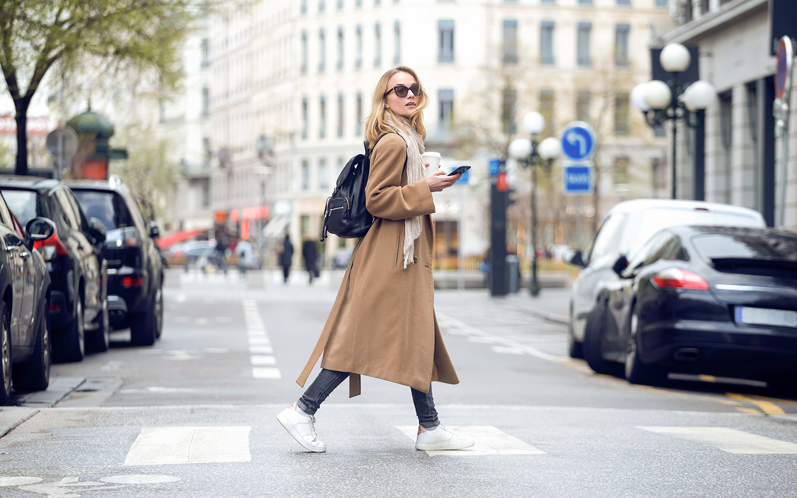 A woman who has worn a trench coat, looking sideways while crossing the road by foot
