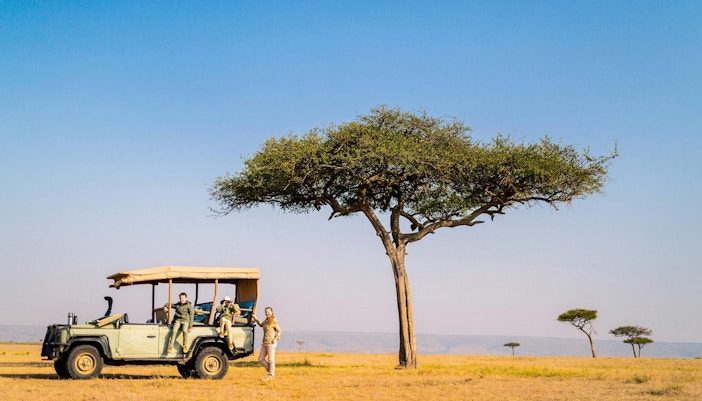 Family on safari in open jeep near acacia tree in African savanna.
