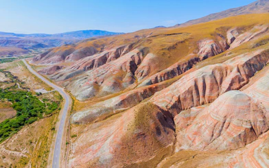 Aerial view of colorful striped hills in Candy Cane Mountains, Azerbaijan, with a road winding through the landscape.