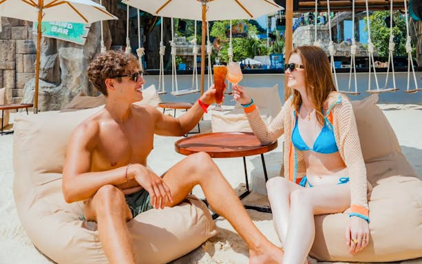 Couple enjoying drinks on beach loungers at Andamanda Phuket Water Park.