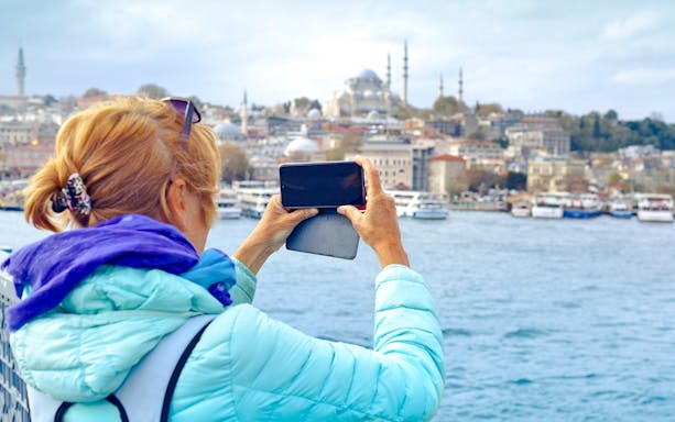 Woman photographing Istanbul landmarks from Galata Bridge.