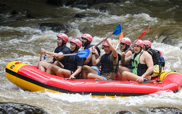 Group rafting on Ayung River in Bali, navigating rapids with paddles raised.