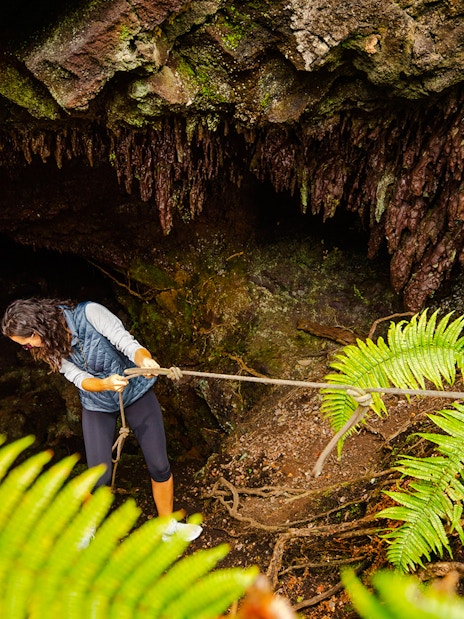 Guests descending into a cave on the Hualalai Volcano during the Hidden Craters Hike.