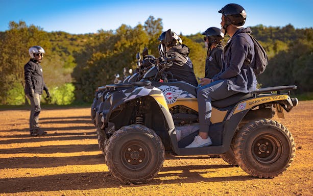 Group preparing for quad tour in Algarve, Portugal, with guide and ATVs on dirt path.