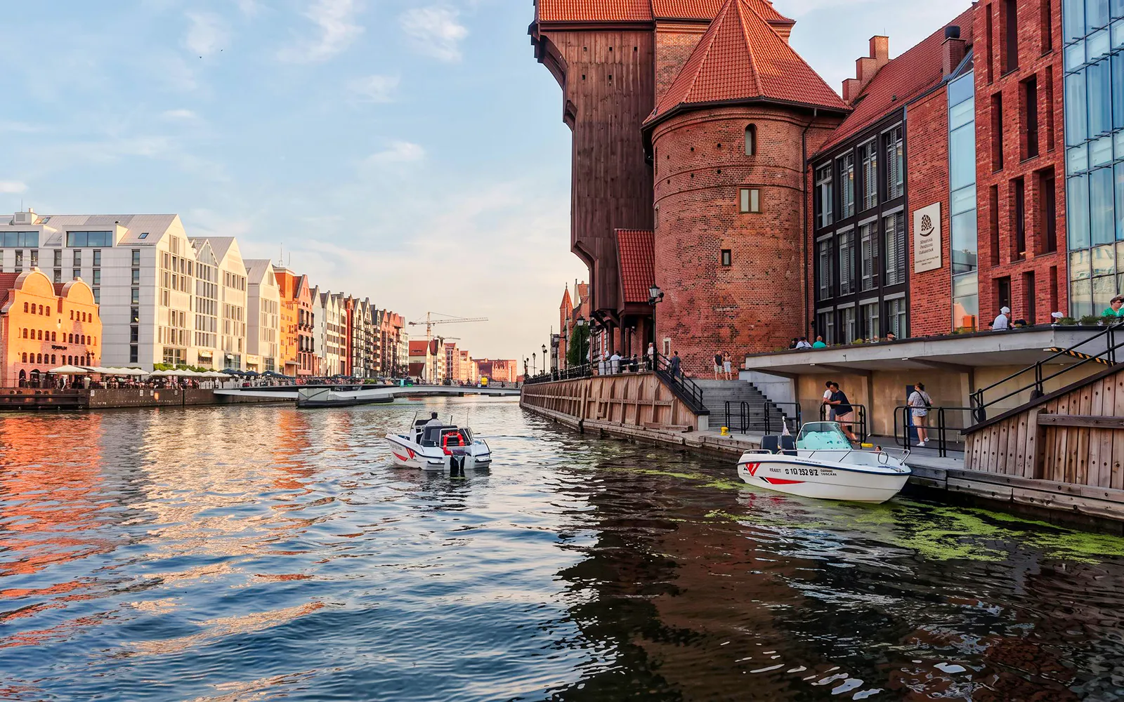 Gdańsk Motława river with electric boat near historic waterfront buildings.