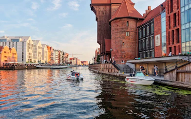 Gdańsk Motława river with electric boat near historic waterfront buildings.