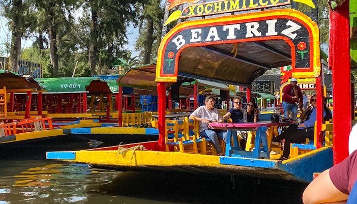 Colorful trajinera boats on Xochimilco canal, Mexico City, with tourists enjoying a guided tour.