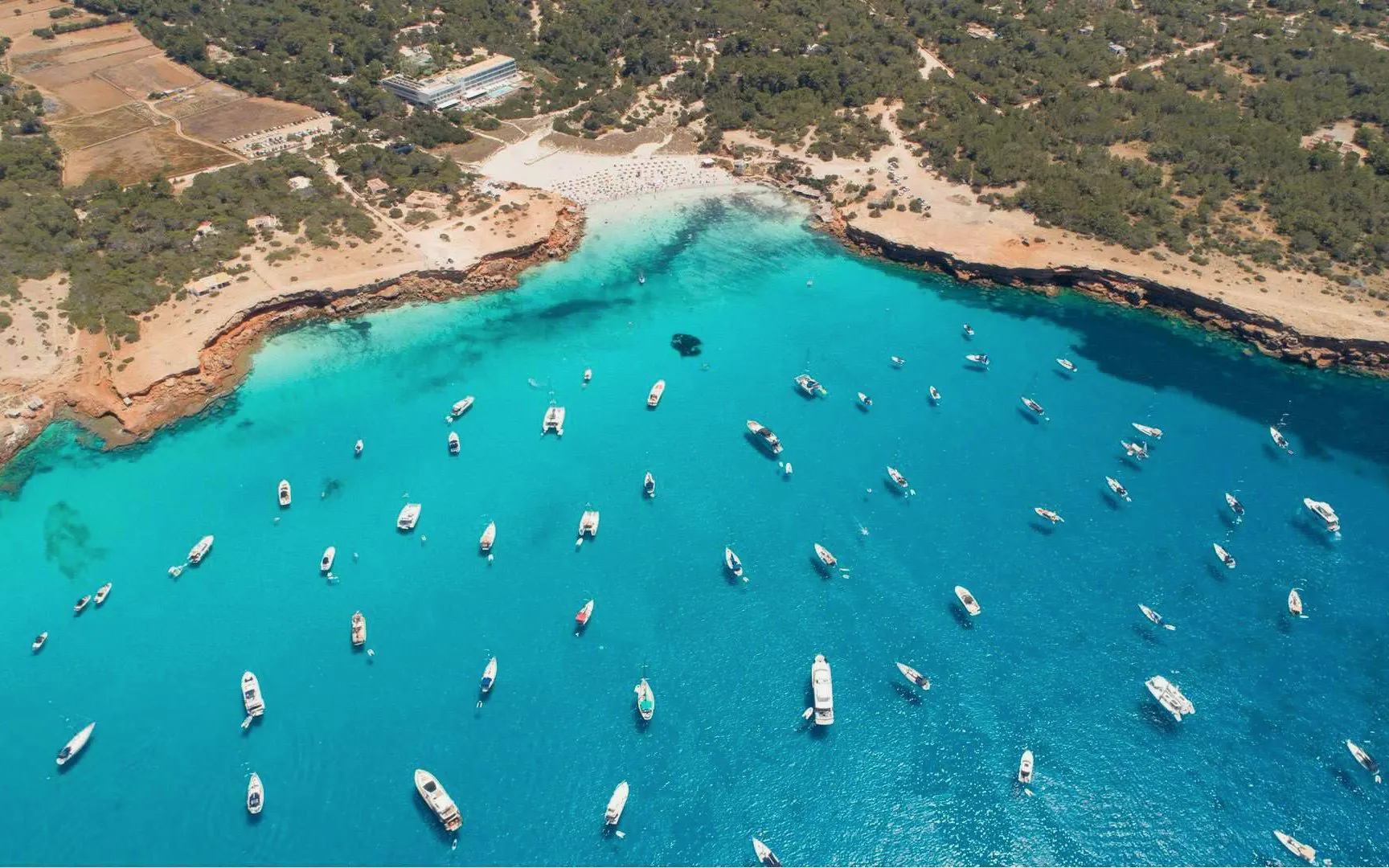 Boats anchored in turquoise waters near Formentera coast, viewed from above.